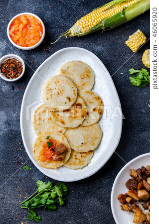 COLOMBIAN FOOD. Maize AREPAS and fried pork chicharron ans colombian tomato sauce. Top view. Black COLOMBIAN FOOD. Maize AREPAS and fried pork chicharron ans colombian tomato sauce. Top view. Black 46065920