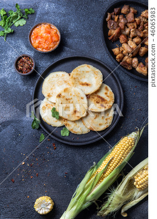 COLOMBIAN FOOD. Maize AREPAS and fried pork chicharron ans colombian tomato sauce. Top view. Black COLOMBIAN FOOD. Maize AREPAS and fried pork chicharron ans colombian tomato sauce. Top view. Black 46065983