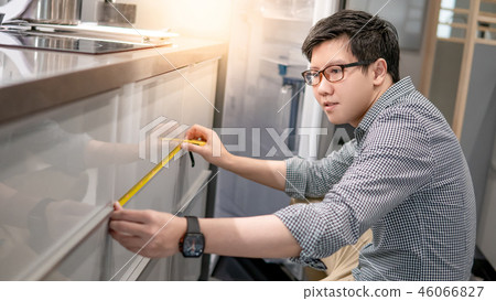 Asian man using tape measure on kitchen counter 46066827