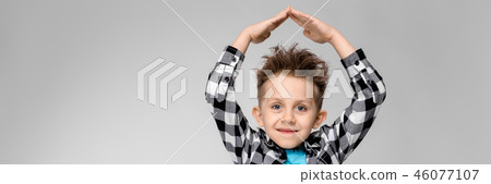 A handsome boy in a plaid shirt, blue shirt and jeans stands on a gray background. The boy folded A handsome boy in a plaid shirt, blue shirt and jeans stands on a gray background. The boy folded 46077107