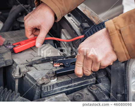 Man recharging a dead car battery in winter time using start-charger. Close up hands of a man with Man recharging a dead car battery in winter time using start-charger. Close up hands of a man with 46080098