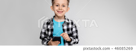 A handsome boy in a plaid shirt, blue shirt and jeans stands on a gray background. The boy is A handsome boy in a plaid shirt, blue shirt and jeans stands on a gray background. The boy is 46085269