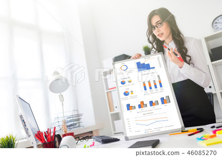 A beautiful young girl stands near an office desk and draws a magnetic marker on the magnetic board. A beautiful young girl stands near an office desk and draws a magnetic marker on the magnetic board. 46085270