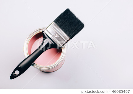 Brush with black handle on open can of pink paint on grey background. Brush with black handle on open can of pink paint on grey background. 46085407