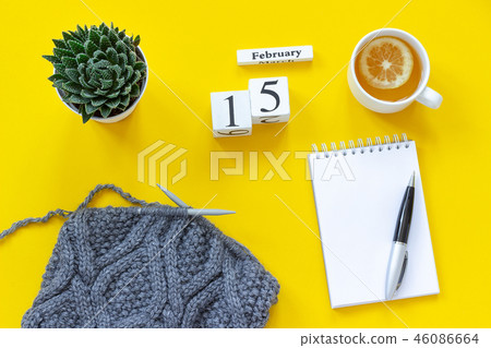 Wooden cubes calendar February 15th. Cup of tea with lemon, empty open notepad for text. Pot with Wooden cubes calendar February 15th. Cup of tea with lemon, empty open notepad for text. Pot with 46086664