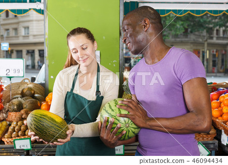 Smiling seller woman is helping man choose melone and watermelon 46094434