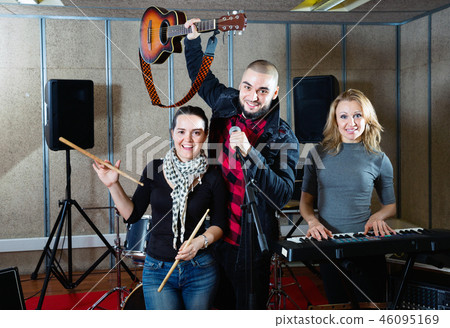Three bandmates posing together with musical instruments in rehearsal room 46095169