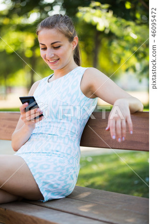 girl sitting on a bench and using mobile in garden 46095472
