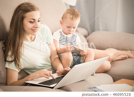 Smiling female is productively working behind laptop while kid playing on tablet 46095528