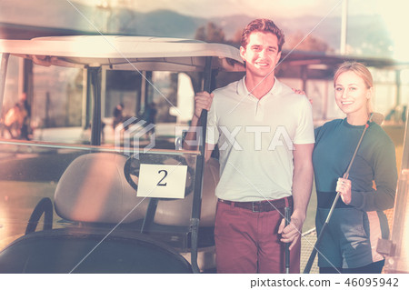 Male and female golf players driving golf cart at golf course Male and female golf players driving golf cart at golf course 46095942