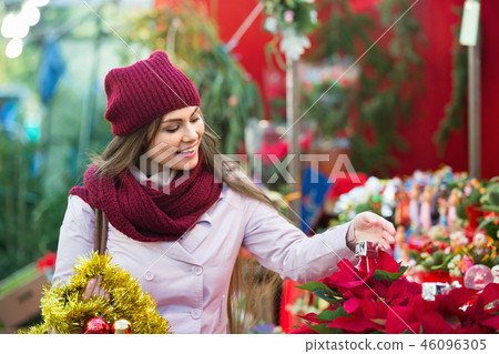 Smiling young woman buying floral compositions at Christmas market Smiling young woman buying floral compositions at Christmas market 46096305