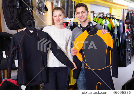 Man and woman are standing with modern diving costumes and flippers in the store. Man and woman are standing with modern diving costumes and flippers in the store. 46096886