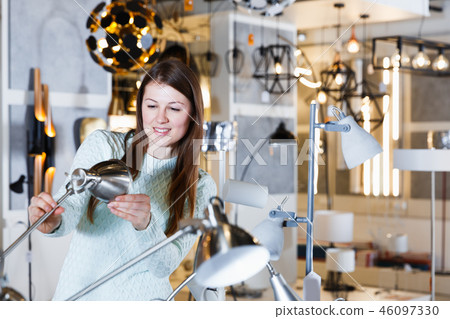 Young female touching desk lamp in furniture showroom Young female touching desk lamp in furniture showroom 46097330