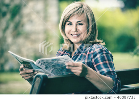 Portrait of mature woman sitting on bench and reading book in garden 46097735