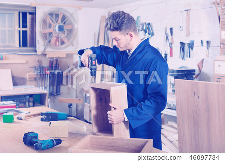Male worker finishing to drill drawer Male worker finishing to drill drawer 46097784