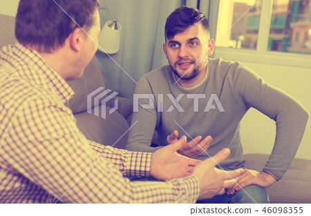 Happy male enjoying сonversation with friend on sofa Happy male enjoying сonversation with friend on sofa 46098355