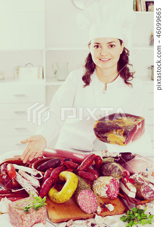 Girl cook costs near table on which sausages and smoked meat Girl cook costs near table on which sausages and smoked meat 46099665