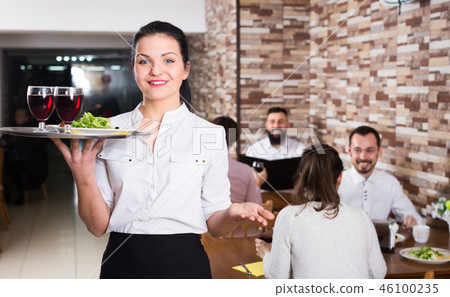 Smiling female waiter greeting customers at table 46100235