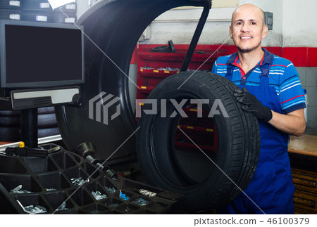 Mature male technician holding car wheel ready to work with balancing machinery at workshop Mature male technician holding car wheel ready to work with balancing machinery at workshop 46100379
