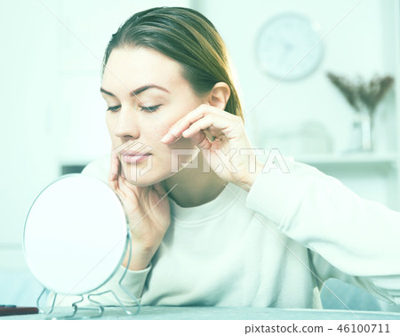 Smiling female is looking on her skin in the mirror 46100711