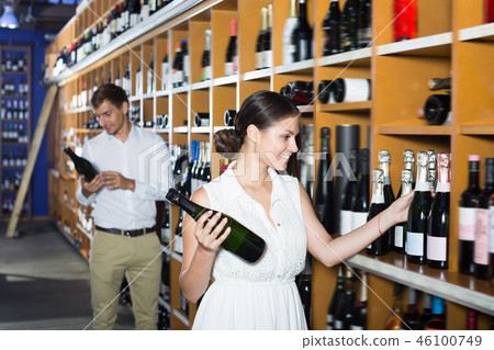 Glad adult woman choosing bottle in wine shop Glad adult woman choosing bottle in wine shop 46100749
