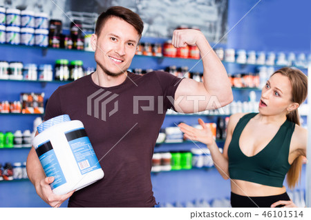 Athletic guy showing muscles while standing in store of sports nutritional supplements Athletic guy showing muscles while standing in store of sports nutritional supplements 46101514