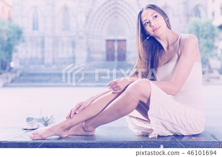 portrait of young adult girl in evening apparel sitting with sandals in european town portrait of young adult girl in evening apparel sitting with sandals in european town 46101694
