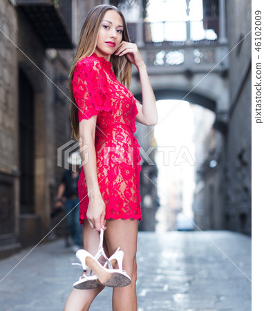 portrait of young female in sexually red gown with pumps in hands standing in town portrait of young female in sexually red gown with pumps in hands standing in town 46102009