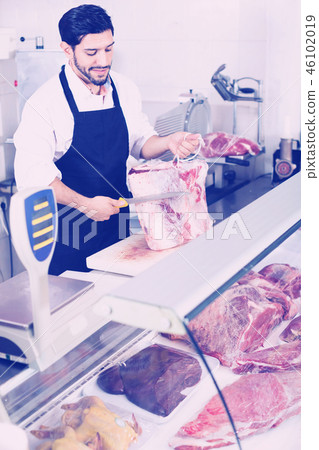 Adult butcher is cutting meat for seller to clients indoors. Adult butcher is cutting meat for seller to clients indoors. 46102019