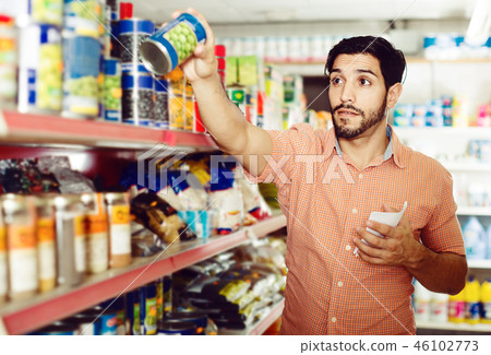 Man is choosing conserved peas using note list in supermarket. 46102773