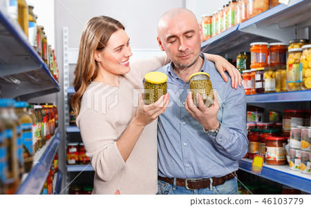 Positive family couple holding canned goods in the food store 46103779