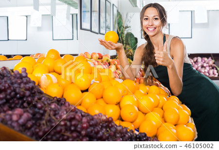 Cheerful woman seller holding orange in hand Cheerful woman seller holding orange in hand 46105002