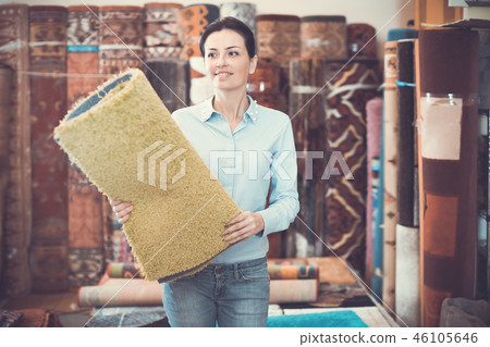 Cheerful woman customer choosing colored carpet Cheerful woman customer choosing colored carpet 46105646