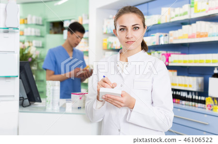 Young female pharmacist is attentively checking medicine to notebook Young female pharmacist is attentively checking medicine to notebook 46106522