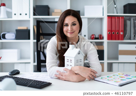 Young girl sitting at the table and holding hands near the layout of the house. 46110797
