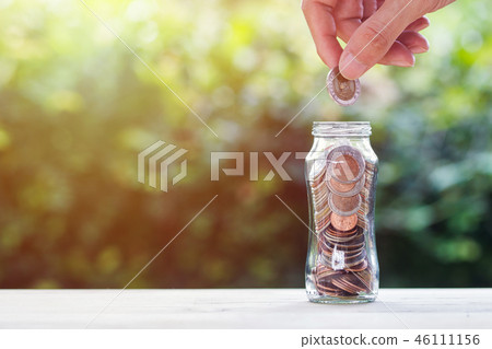 Hand holding coin over coins in glass jar. Hand holding coin over coins in glass jar. 46111156