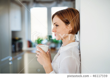 A young woman with cup of coffee standing indoors, leaning on a wall. A young woman with cup of coffee standing indoors, leaning on a wall. 46117339