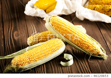 Kitchen table with raw and grilled sweet corn cob 46120653