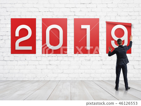 A businessman putting up posters with numbers 2, 0, 1, and 9 on a white brick wall. A businessman putting up posters with numbers 2, 0, 1, and 9 on a white brick wall. 46126553