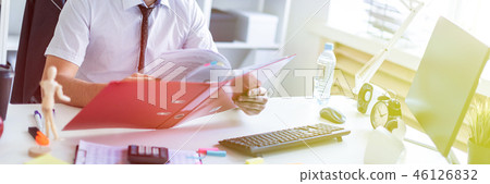 A man is sitting at a table in the office, working with documents and a computer. 46126832