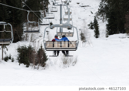 Two skiers on chair-lift in gray day Two skiers on chair-lift in gray day 46127103