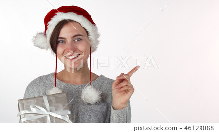 Happy beautiful woman in Christmas hat holding a present, pointing at copyspace 46129088