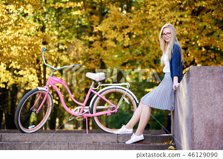 Blond long-haired attractive girl on pink lady bicycle in sunny autumn park on trees background. 46129090