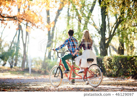 Young couple, handsome man and attractive woman on tandem bike in sunny summer park or forest. 46129097