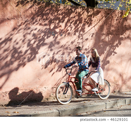 Tourist couple, bearded man and blond woman on tandem bicycle on background of red crackled wall. 46129101