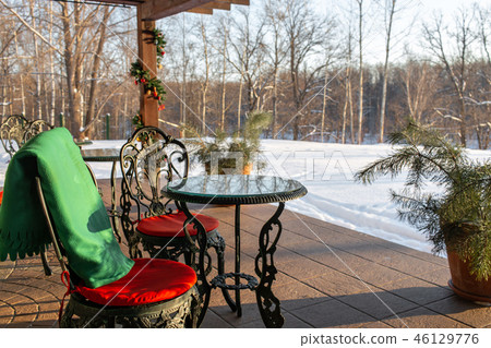 Cast iron chairs and tables with pillows and a blanket on restaurant terrace. Winter landscape of 46129776