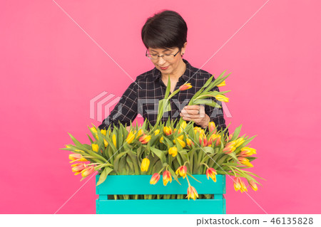 Middle-aged caucasian woman with box of tulips in pink studio. 46135828