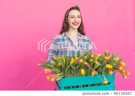 Happy caucasian young woman with box of yellow tulips on pink background with copy space 46136087