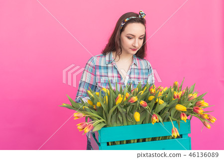 Happy caucasian young woman with box of yellow tulips on pink background 46136089