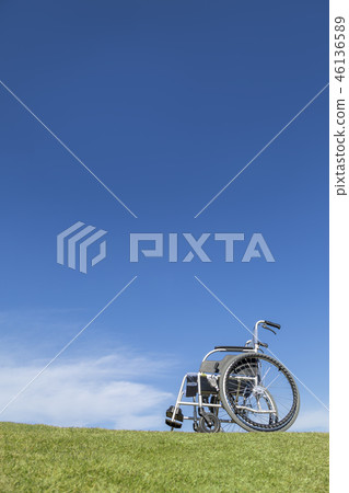 Unmanned wheelchair placed on the grass against the blue sky background. Welfare, care, illness, disabled person, image of old age 46136589